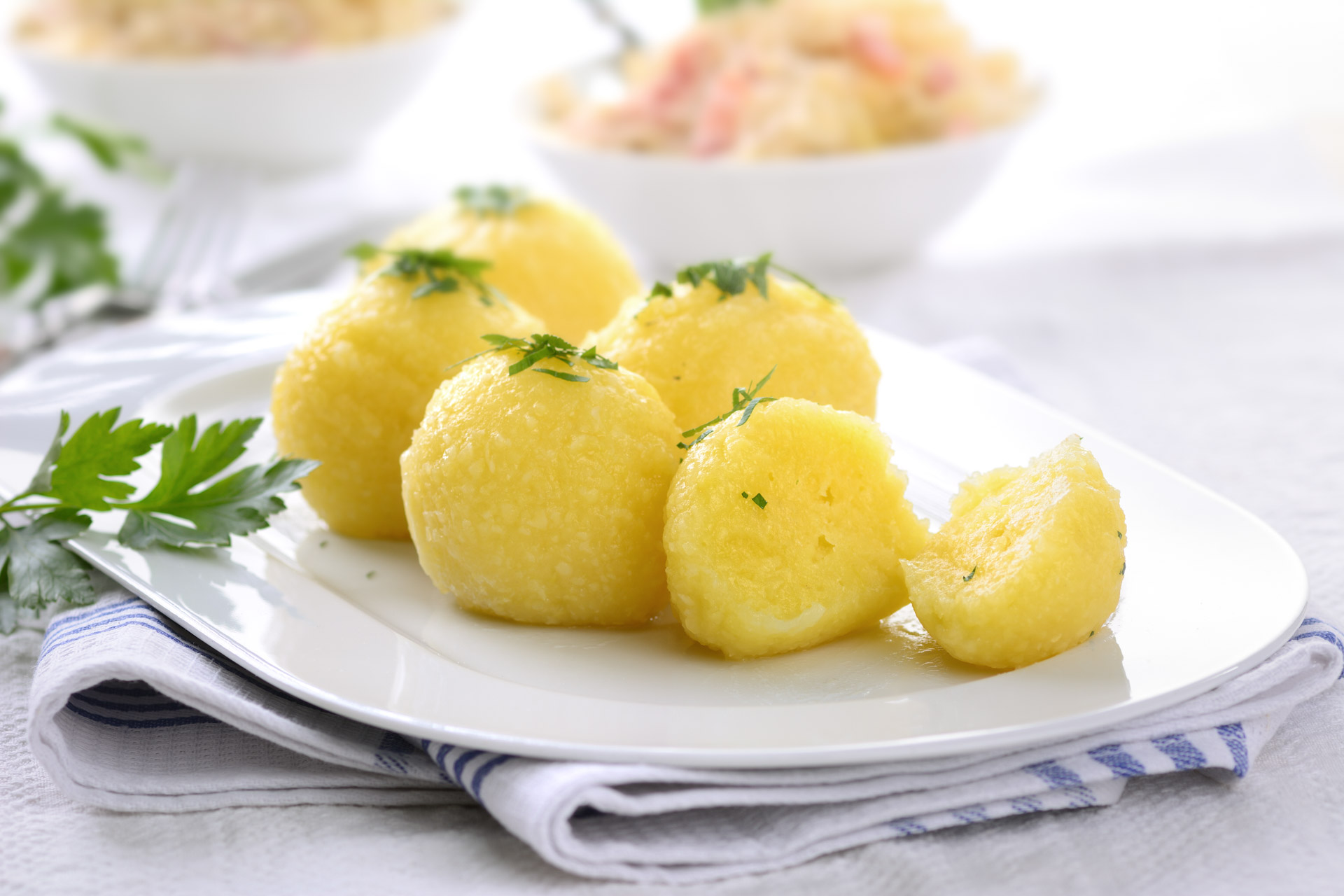 Kartoffelknödel auf einem Teller, Sauerkraut mit Schinken ist im Hintergrund
