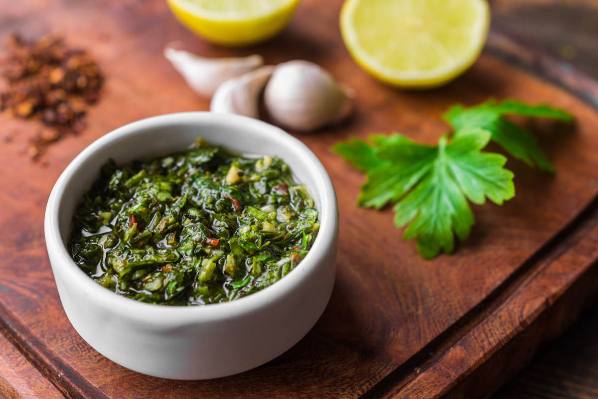 Foto traditioneller argentinischer Chimichurri Sauce auf einem Holzbrett mit Chili-Flocken, und Knoblauch-Zehen
